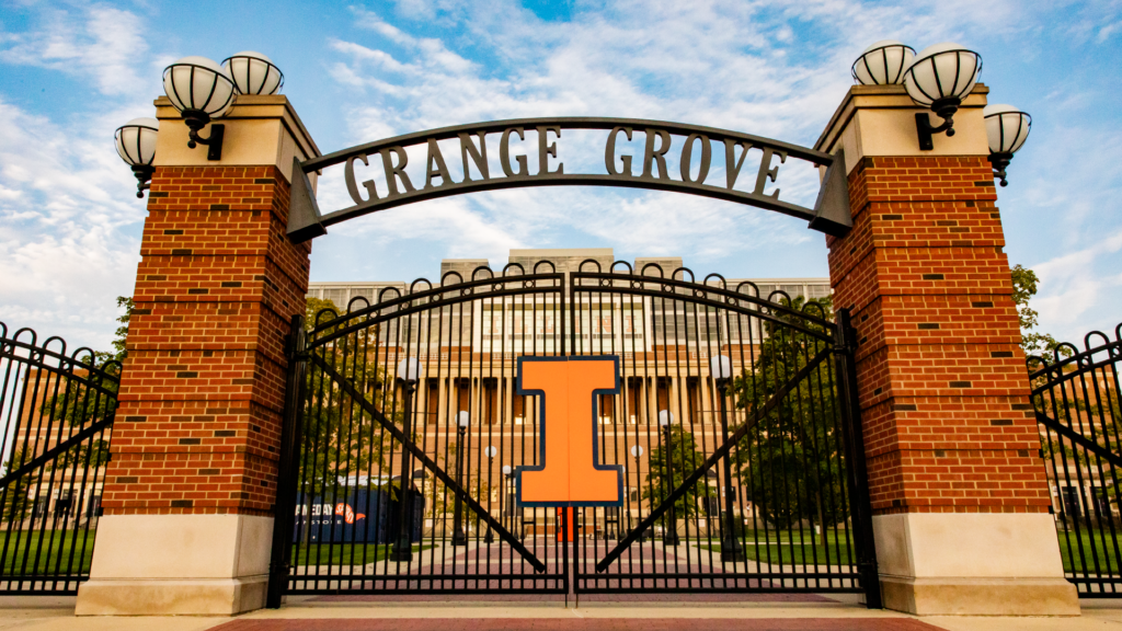 The entrance to Grange Grove, featuring a large metal arch with the name displayed prominently, flanked by brick pillars and decorative lamps, with a University of Illinois Block I logo at the center.