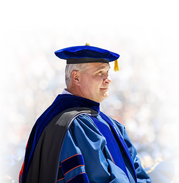 A faculty member sitting in their regalia at the commencement ceremony.